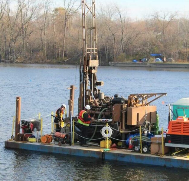Drill crew chiefs obtaining soil samples for environmental testing on the Grand River with drill rig mounted on barge