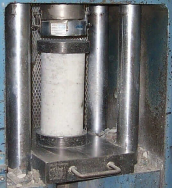 Concrete cylinder in a compression machine to perform concrete strength testing